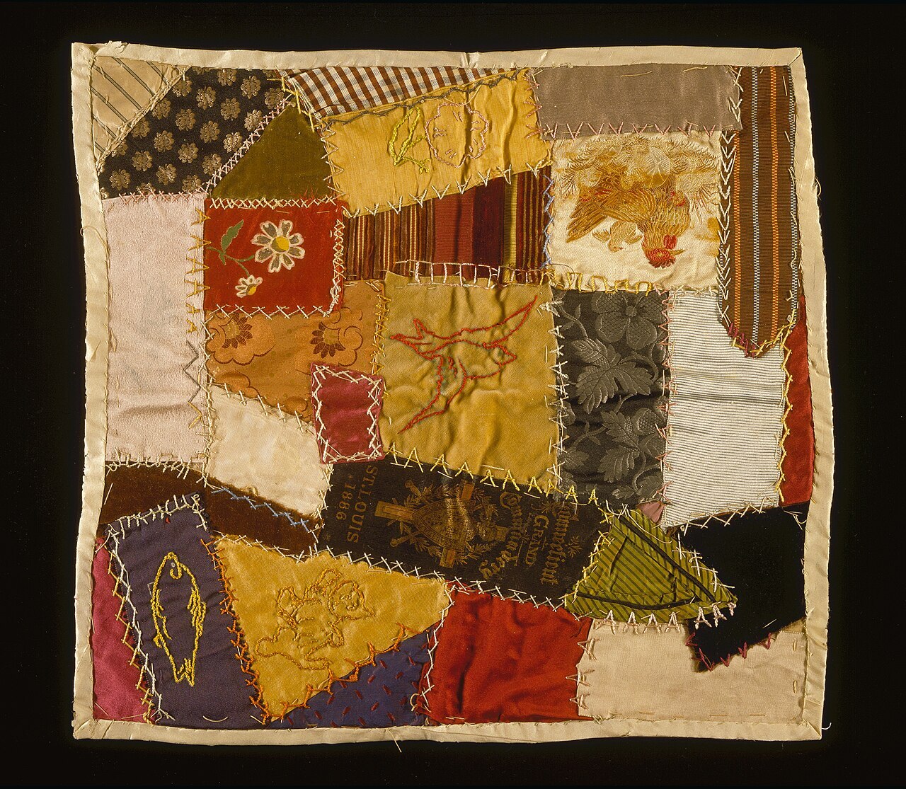 A small crazy quilt of silk and velvet scraps joined with bright feather stitching, an embroidered bird at its center